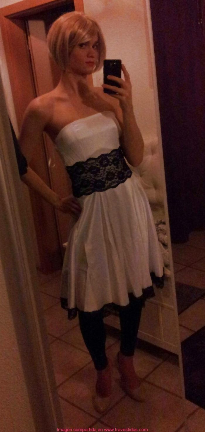 Rubia travestida se toma una selfie usando un vestido blanco